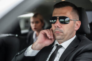 Agent in civilian black suit with handsfree earpiece radio drive celebrity vip person in the car. Bodyguard and VIP person security protection. Professional police agent special forces